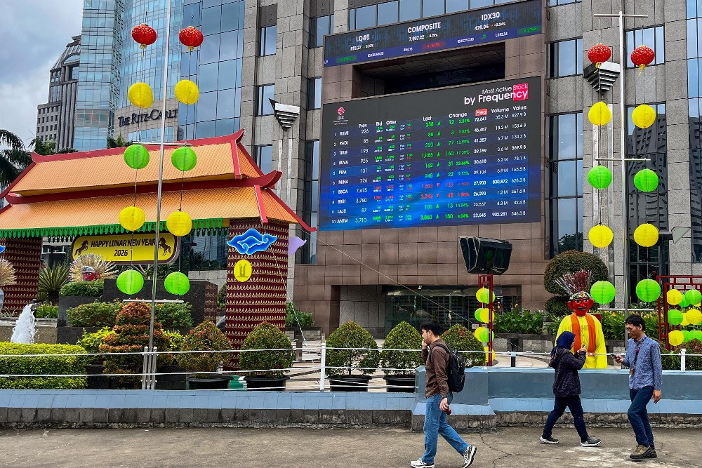 Warga melintas di dekat layar pergerakan saham di gedung BEI di Jakarta, Senin (9/2/2026)./Bisnis/Himawan L. Nugraha