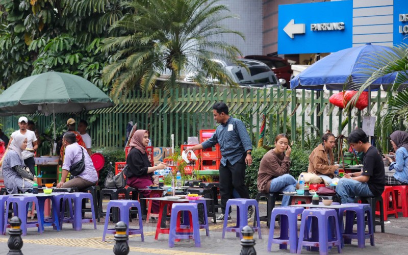 Warga melintas di dekat kedai pedagang kali lima (PKL) di Jakarta, Minggu (4/12). Pemerintah menargetkan penyaluran kredit usaha rakyat atau KUR bersubsidi sebesar Rp450 triliun pada 2023 mendatang. Adapun pemerintah menetapkan tingkat suku bunga sebesar 3% untuk KUR super mikro  dengan plafon di bawah Rp10 juta, kemudian untuk KUR Mikro dan KUR Kecil dengan plafon Rp10 juta - Rp500 juta sebesar 6%, serta plafon Rp500 juta - Rp10 miliar dikenakan bunga 11-12%. Bisnis/Himawan L Nugraha