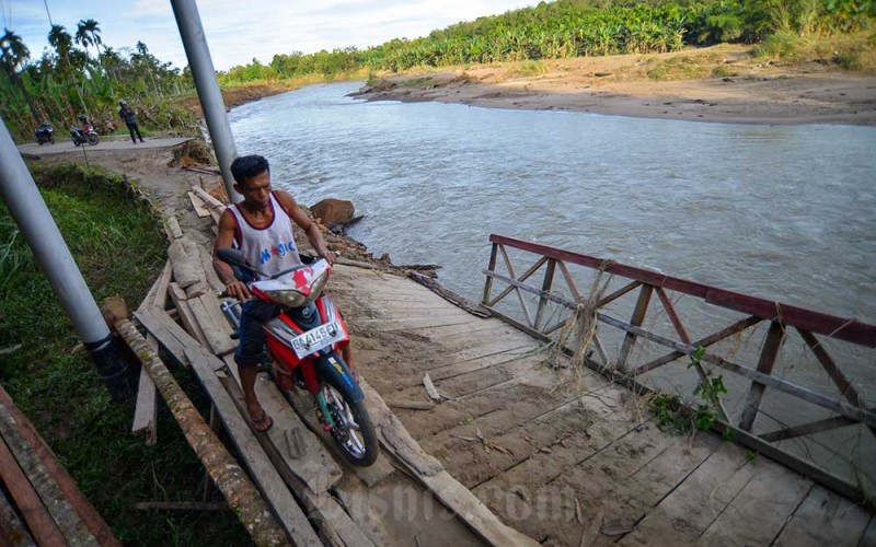 Warga mengendarai motornya melintasi penyeberangan darurat di Nagari Sungai Buluh Timur, Kabupaten Padang Pariaman, Sumatera Barat Kamis (26/1/2023). Jembatan darurat yang dibangun masyarakat itu hancur akibat luapan Sungai Batang Anai dua hari lalu, sehingga warga kembali membuat penyeberangan darurat dari batang kelapa untuk akses antar desa.  ANTARA FOTO/Iggoy el Fitra