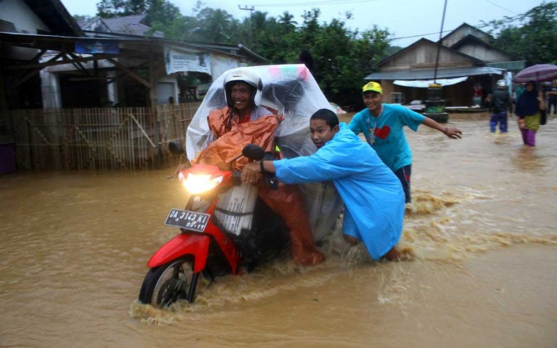 Warga membantu pengendara motor melintasi jalan yang terendam banjir di Desa Bulayak, Kabupaten Hulu Sungai Tengah, Kalimantan Selatan, Kamis (16/3/2023). Akibat curah hujan tinggi mengakibatkan sungai Hantakan meluap dan merendam sejumlah desa di Kabupaten Hulu Sungai Tengah. ANTARA FOTO/Bayu Pratama S