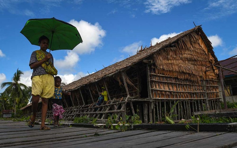 Warga berjalan melintasi rumah adat Jew di Kampung Ewer, Distrik Agats, Kabupaten Asmat, Papua Selatan, Rabu (31/5/2023). Rumah adat yang menggunakan bahan-bahan alami yang diambil langsung dari alam tersebut dibangun untuk tempat tinggal para laki-laki Suku Asmat yang belum menikah. ANTARA FOTO/Aditya Pradana Putra