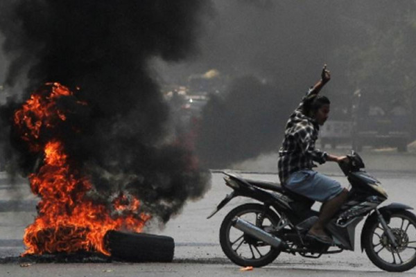 Seorang pria mengacungkan salam tiga jari, simbol perlawanan sipil terhadap kudeta dan junta militer Myanmar, ketika melewati ban terbakar sewaktu unjuk rasa menentang kudeta di Mandalay, Myanmar, 1 April 2021./Antara/Reuters-Stringer
