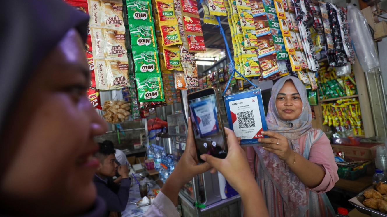 Pedagang mitra UMKM Bank Raya melayani pembeli yang membayar menggunakan fasilitas pindai QRIS pada fitur Saku Bisnis mobile banking Raya di Jakarta, Senin (18/11/2024).  (Bisnis/Himawan L. Nugraha)