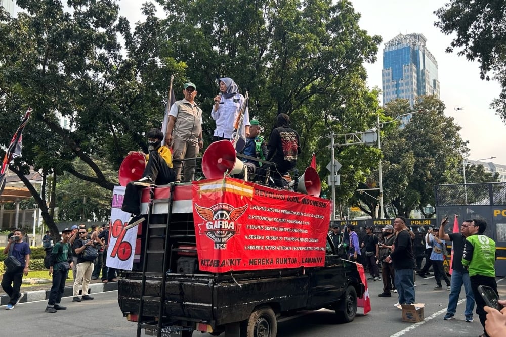 Massa demo ojol mulai berdatangan di Jalan Medan Merdeka Selatan, Jakarta, dengan mobil komando dan spanduk berisi tuntutan, pada Senin (21/7/2025) - BISNIS/Pernita Hestin Untari